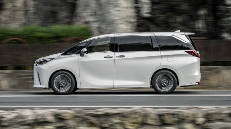 White Lexus LM driving on a road next to a rocky wall