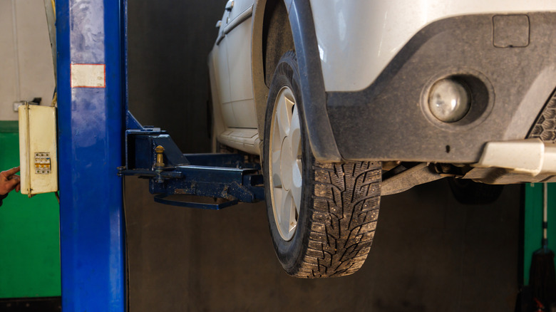 A silver car lifted on elevator at maintenance in auto repair shop.