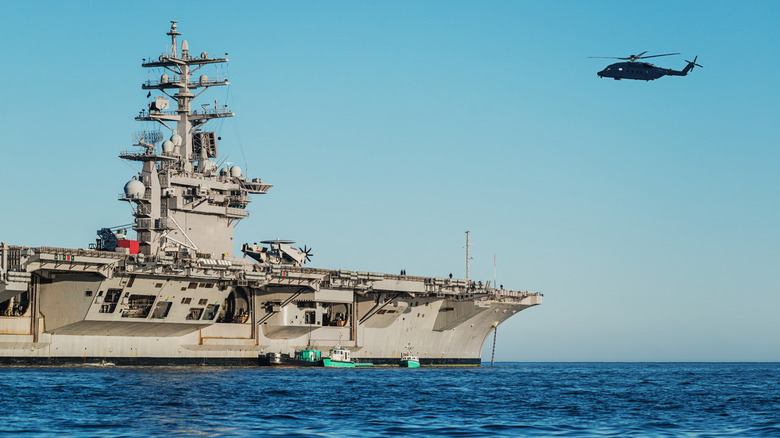 A large naval ship in sea with helicopter approaching