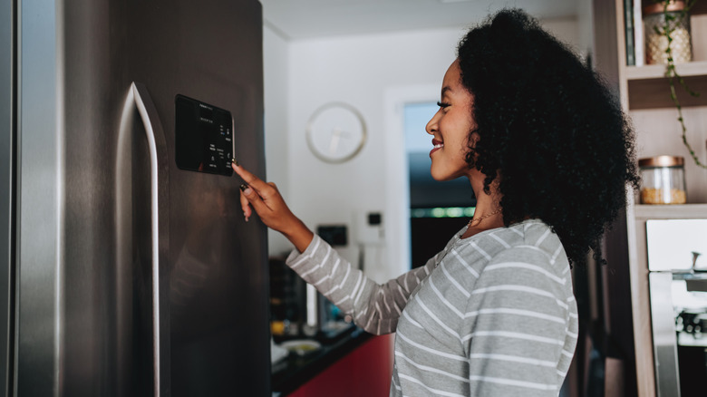 A person adjusts the settings on the front of a smart refrigerator.