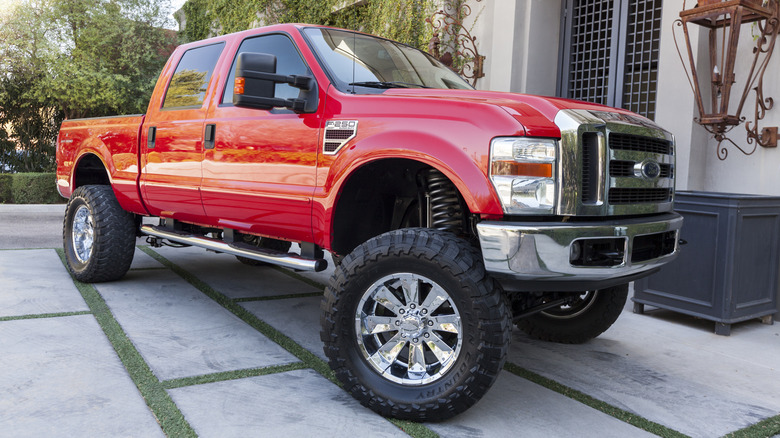 Front 3/4 view of a red 2009 Ford F-250 with a lift kit, aftermarket wheels and M/T tires parked on a driveway