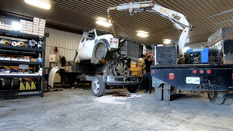 A crane picking up a Ford pickup truck cab in a repair shop.