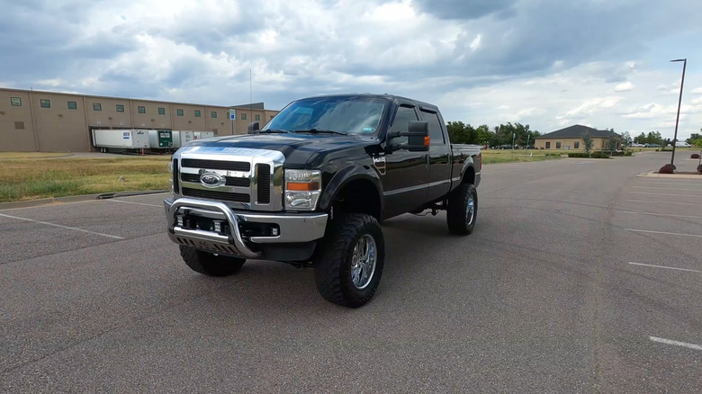 A 2008 Ford F-250 in black, with a chrome bull bar and a lift kit on a large, mostly empty parking lot, front 3/4 view