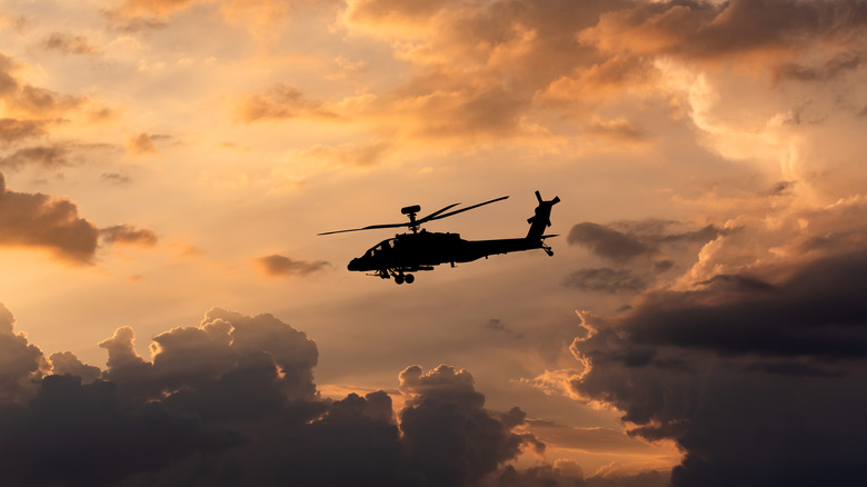 An Apache AH-64 helicopter flying in the sky at sunset