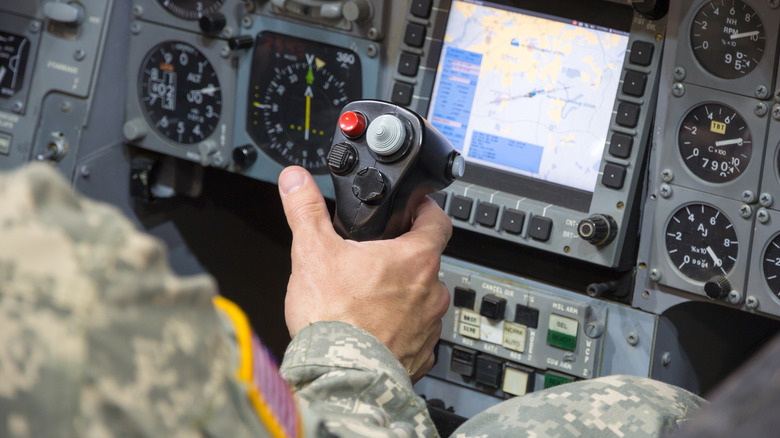 U.S. soldier's hand rests on control stick with red pickle button centered in a military jet simulator