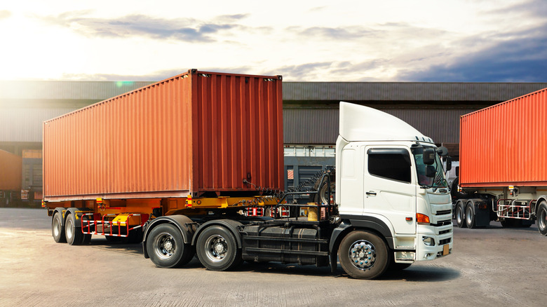 White semi tractor pulling rusted shipping container