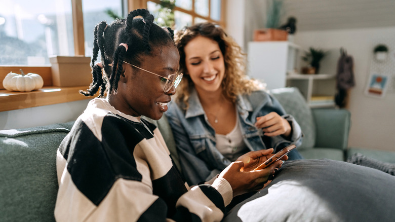 Una mujer negra y una mujer blanca que usa una aplicación de citas y sonriendo