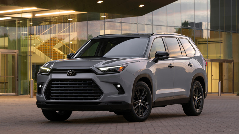 Gray 2026 Toyota Grand Highlander in front of a glass-fronted building.