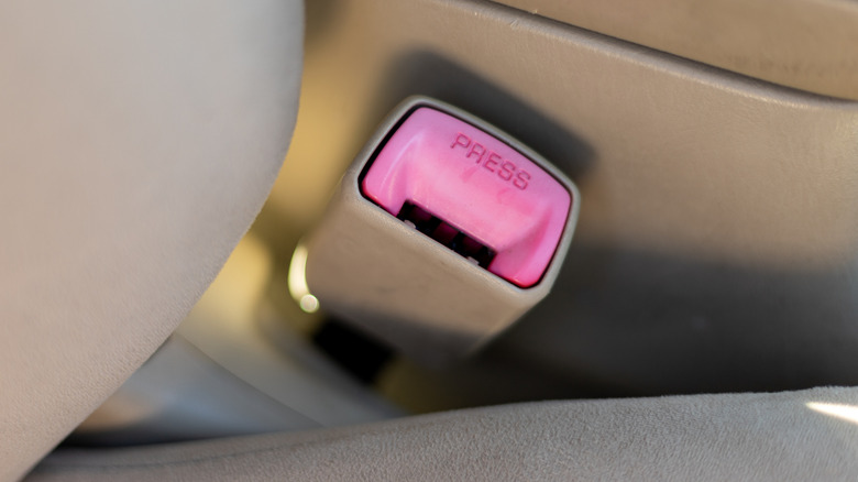 Passenger side seatbelt clip in a vehicle with a tan interior.