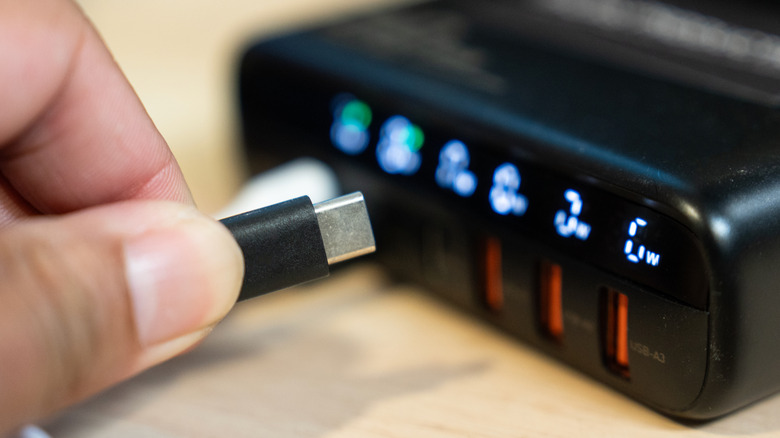 A USB-C cable being held up to a range of USB ports on a portable battery.