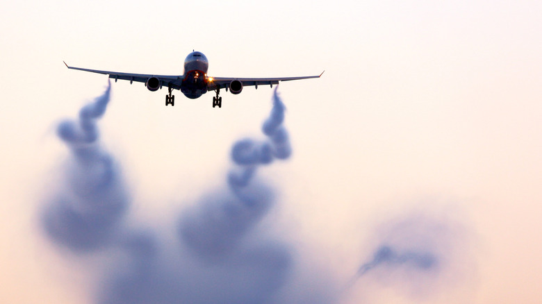 Commercial jet in flight with visible vortices trailing from extended flaps