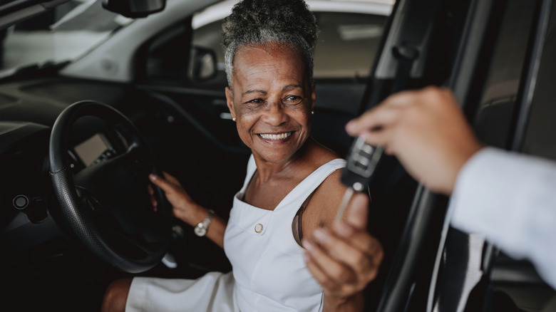 A senior woman being handed the key to a car while at a dealership