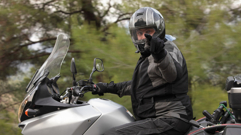 Man on a motor cycle with helmet pointing at camera