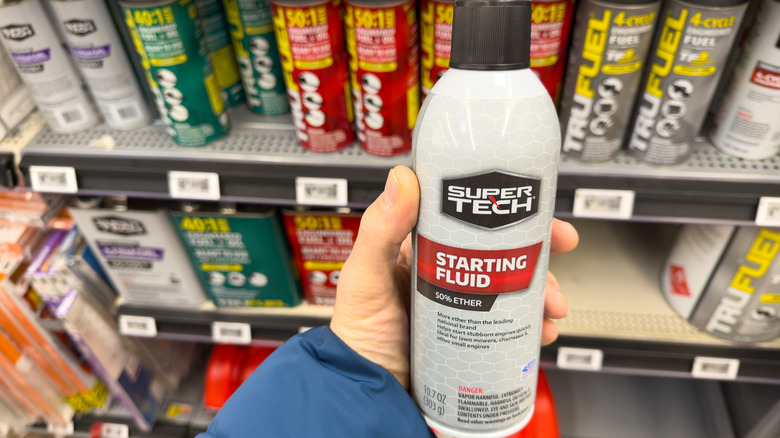 Hand holding bottle of starting fluid in the corresponding aisle of an automotive store.