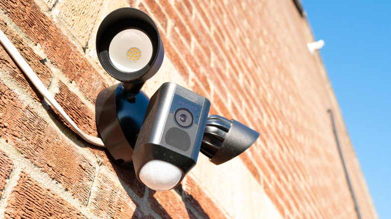 A security camera with sensors on the side of a brick wall.