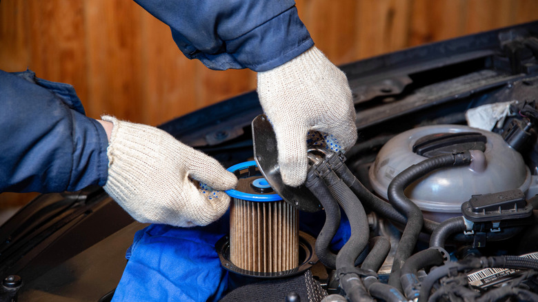 A mechanic takes out an old, dirty fuel filter after refueling with low-quality fuel.