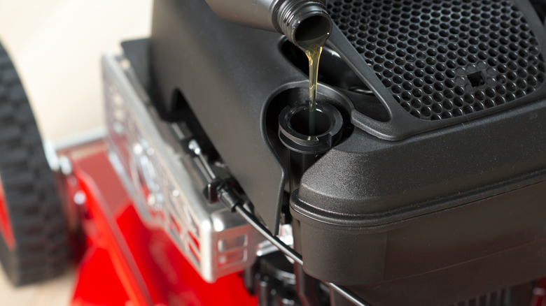 A person pouring oil into a lawn mower.