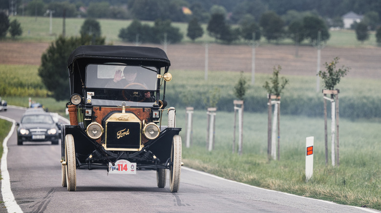 Ford Model T driving on country road with modern traffic, front-view