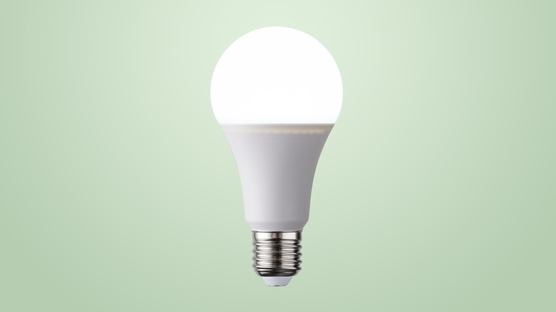 Illuminated White LED Light Bulb Glowing in Mid Air on Light Green Colored Background Front View