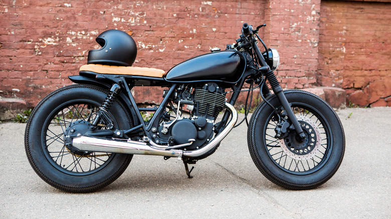 The side view of an unbranded cafe racer motorcycle, black with a tan seat, black helmet on the seat