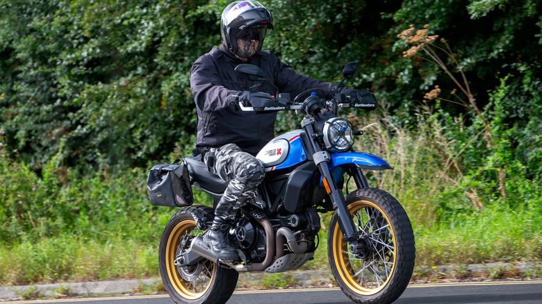 Mman riding  blue Ducati Scrambler on forest road