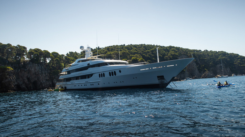 A pair of kayakers are seen paddling past a luxury yacht