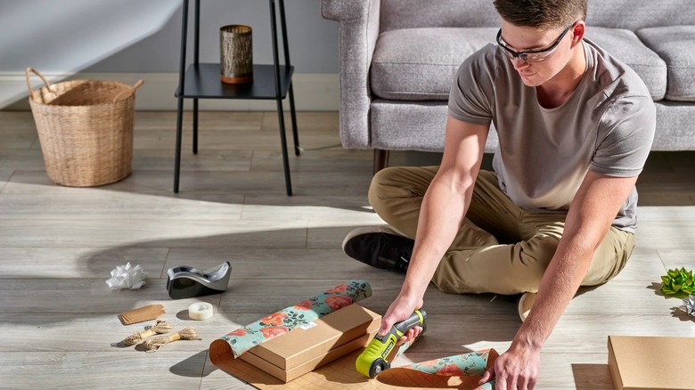 Person on floor using Ryobi USB Lithium Power Cutter to cut wrapping paper