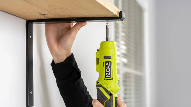 person using Ryobi electric screwdriver on shelf