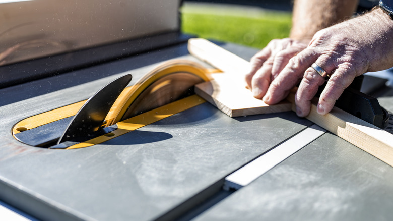 A man making a small cut using a table saw with hands close to the blade