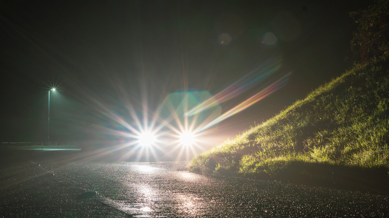 Car with high beams parked next to a small hill at night