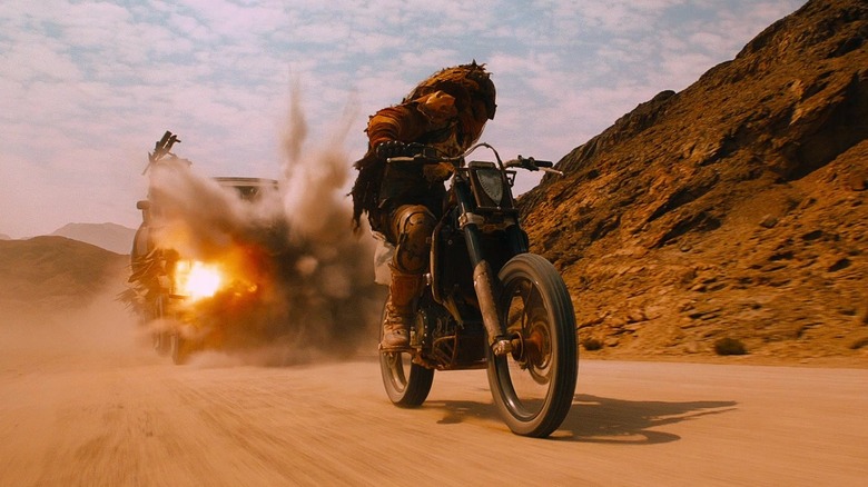 Motorcyclist riding in front of exploding car in desert