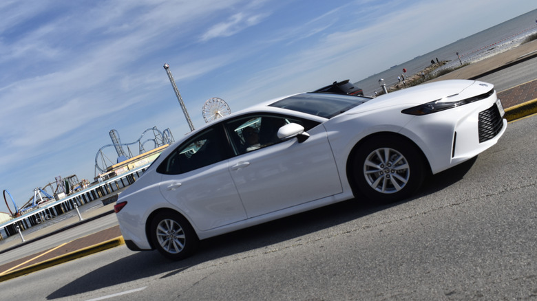 Side view of white 2025 Toyota Camry LE driving on coastal road.