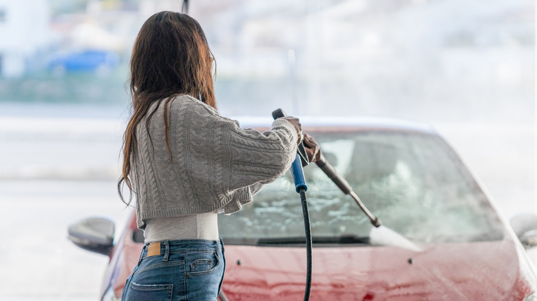 Woman using pressure washer on car windshield