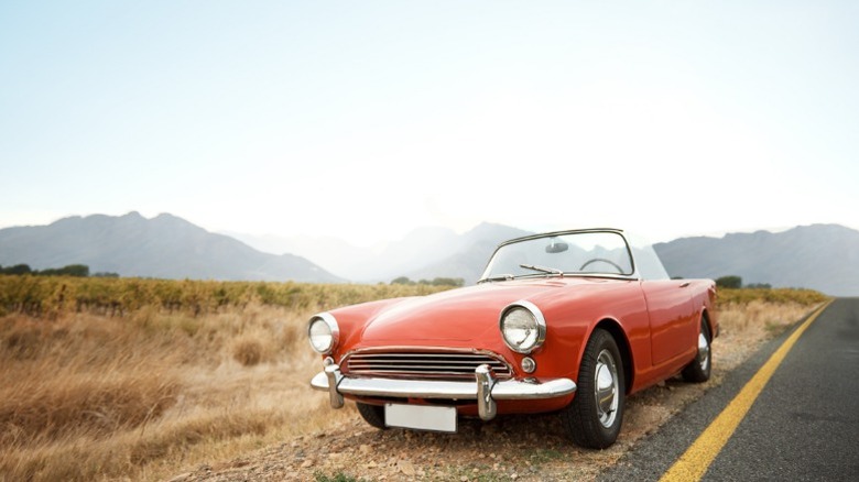 a red classic car parked on the side of a desert highway