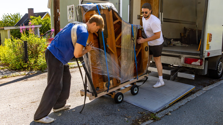 Movers loading heavy item into moving truck on driveway