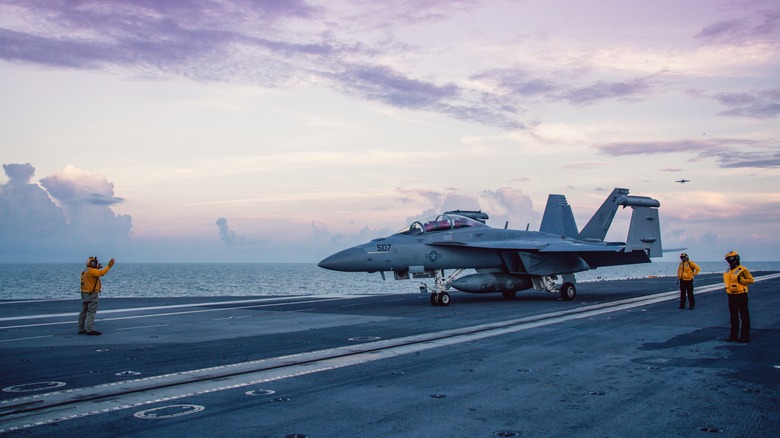 Crew members on the flight deck of an aircraft carrier with a jet