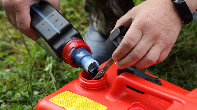 A person pouring two-stroke oil into a container of gasoline