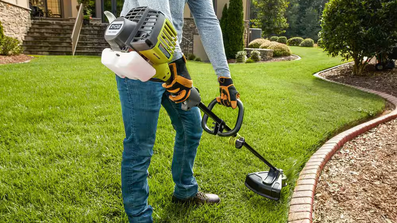 A person using a Ryobi gas string trimmer on a lawn