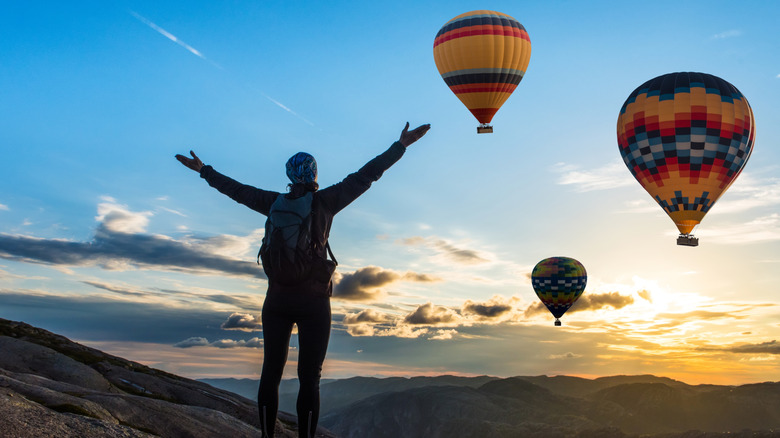 woman on mountains looking at hot air balloons