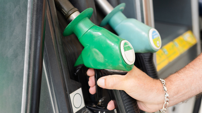 A person reaching for a green fuel pump at a gas station