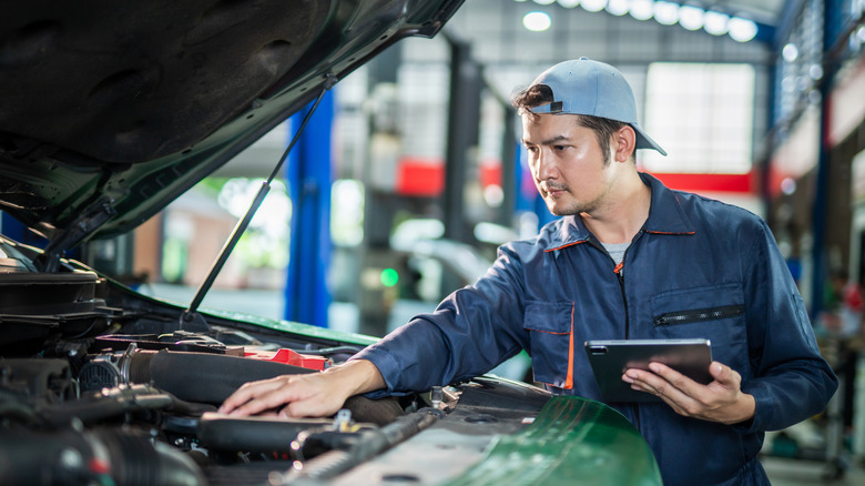 Mechanic working on engine holding a tablet
