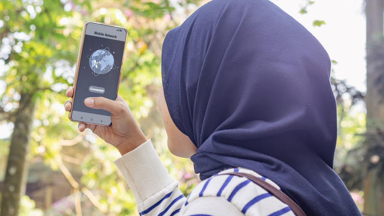 Woman in a blue headscarf connects to network provider on a smartphone outdoors