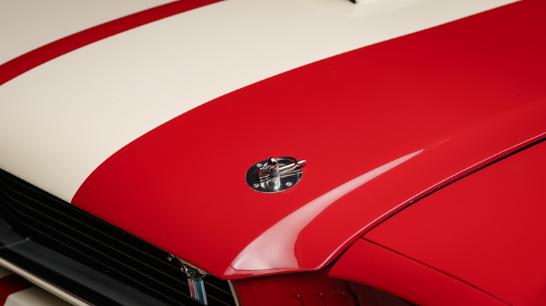 A closeup of a red 1960s Mustang with a hood pin on.