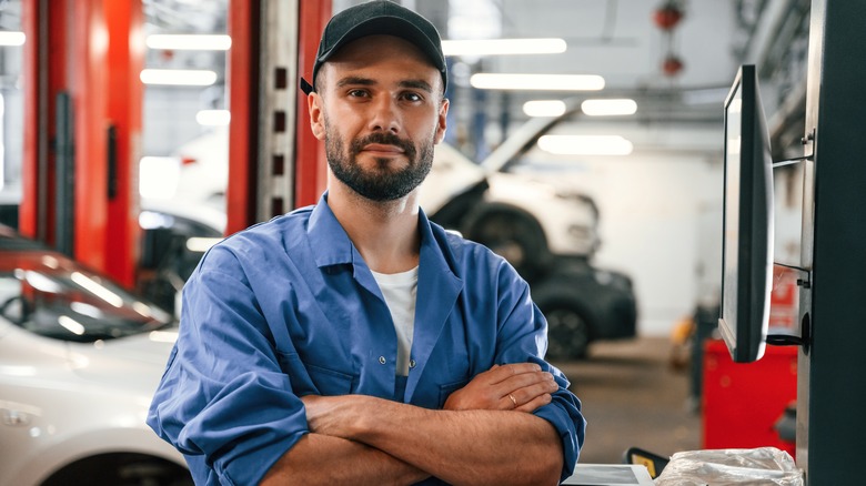 car mechanic standing in front of car with arms crossed
