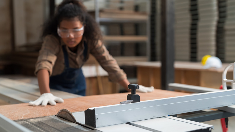 Woman positioning thin board on table saw