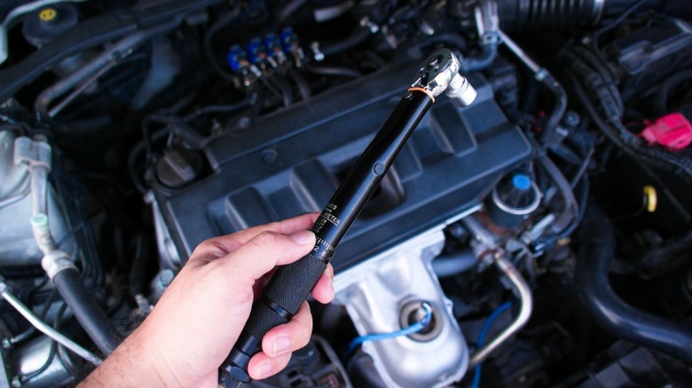 A person holding a torque wrench above a car's engine bay
