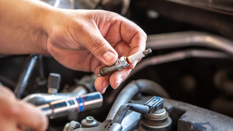 A person holding a used spark plug and a ratchet with a spark plug socket