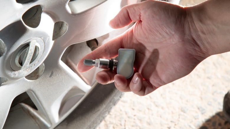 a person holding a tpms sensor in front of a car's wheel