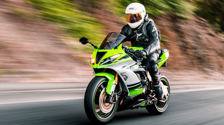 Green Kawasaki motorcycle being driven on the streets with trees in the background