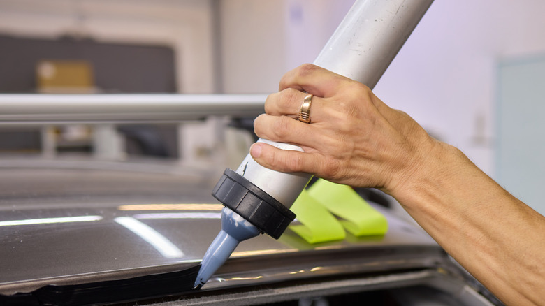 A hand holding a caulking gun while dispensing sealant on the windshield edges